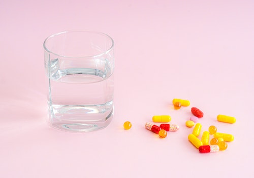 Red and yellow pills with a glass of water